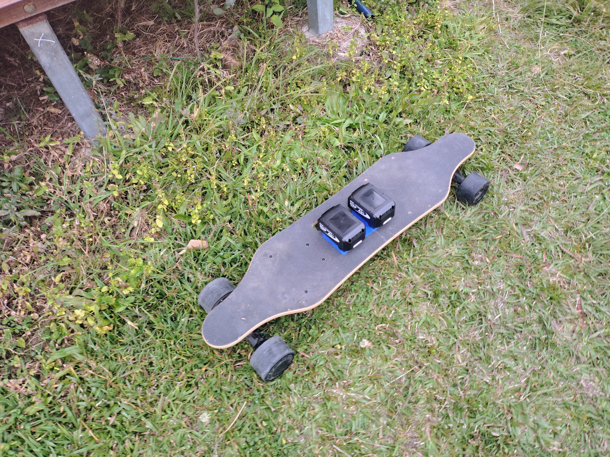 Electric skateboard on grass with visible battery packs